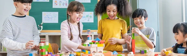 Fünf Kinder spielen mit Bauklötzen in der Kita, im Hintergrund hängen selbstgemalte Bilder