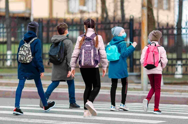 Eine Gruppe Kinder mit Rucksäcken geht über einen Zebrastreifen auf dem Schulweg