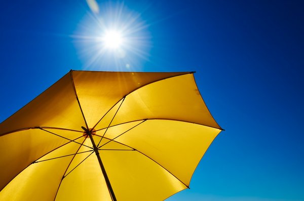 Ein gelber Sonnenschirm vor einem strahlend blauen Himmel mit Sonne.