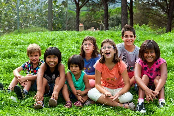 Mehrere Kinder sitzen auf einer Wiese und lachen in die Kamera.
