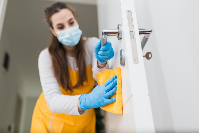 Frau mit Maske reinigt Tür mit Lappen