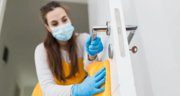 Frau mit Maske reinigt Tür mit Lappen