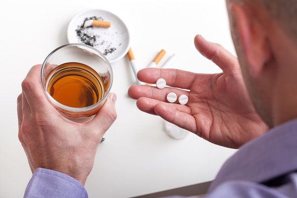 Ein Mann hält in einer Hand ein Glas mit Alkohol und in der anderen Hand Tabletten.