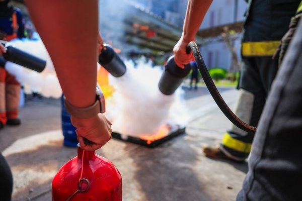 Personen in Schutzkleidung löschen ein Übungsfeuer.
